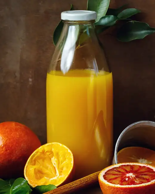 Frisch gepresster Orangensaft in der Glasflasche, daneben halbierte Orangen